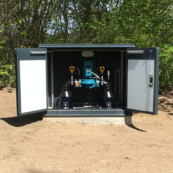 DESMI pumpsystem installeret i et udendørs skab omgivet af træer.