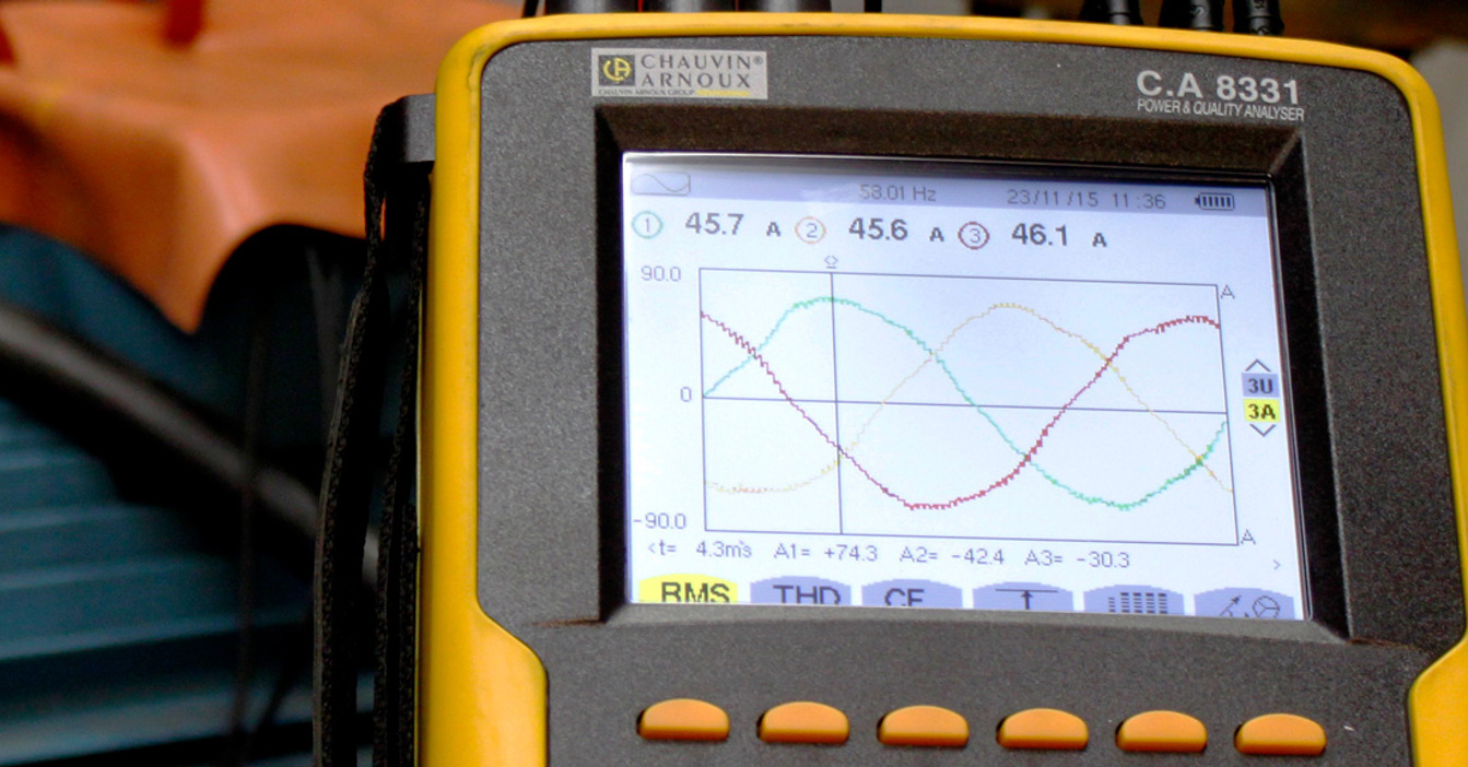 Gul power quality analyzer, der viser bølgeformer nær industrielt udstyr.