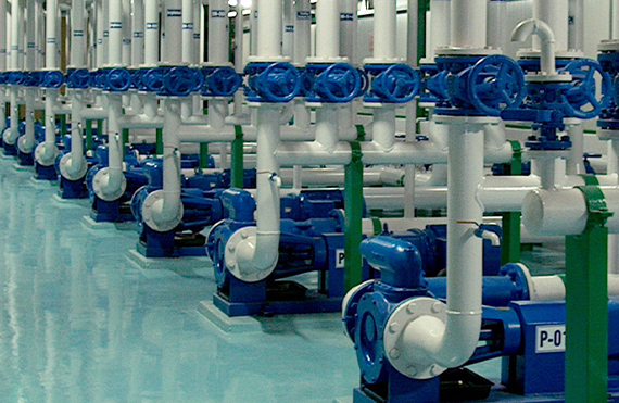 Række af industrielle pumper med blå ventiler og hvide rør til væskehåndtering.