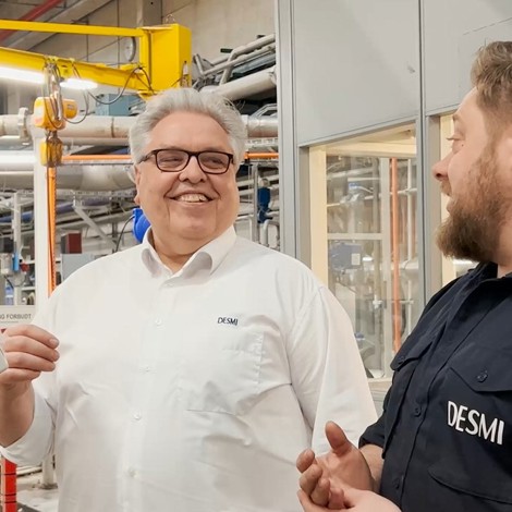 To mænd i DESMI-skjorter taler i et industrielt miljø.