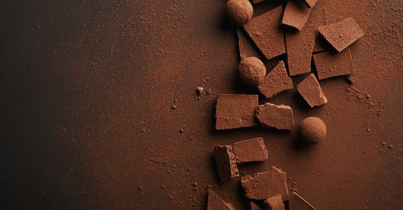 Brudte chokoladestykker og trøfler drysset med kakaopulver på mørk baggrund.