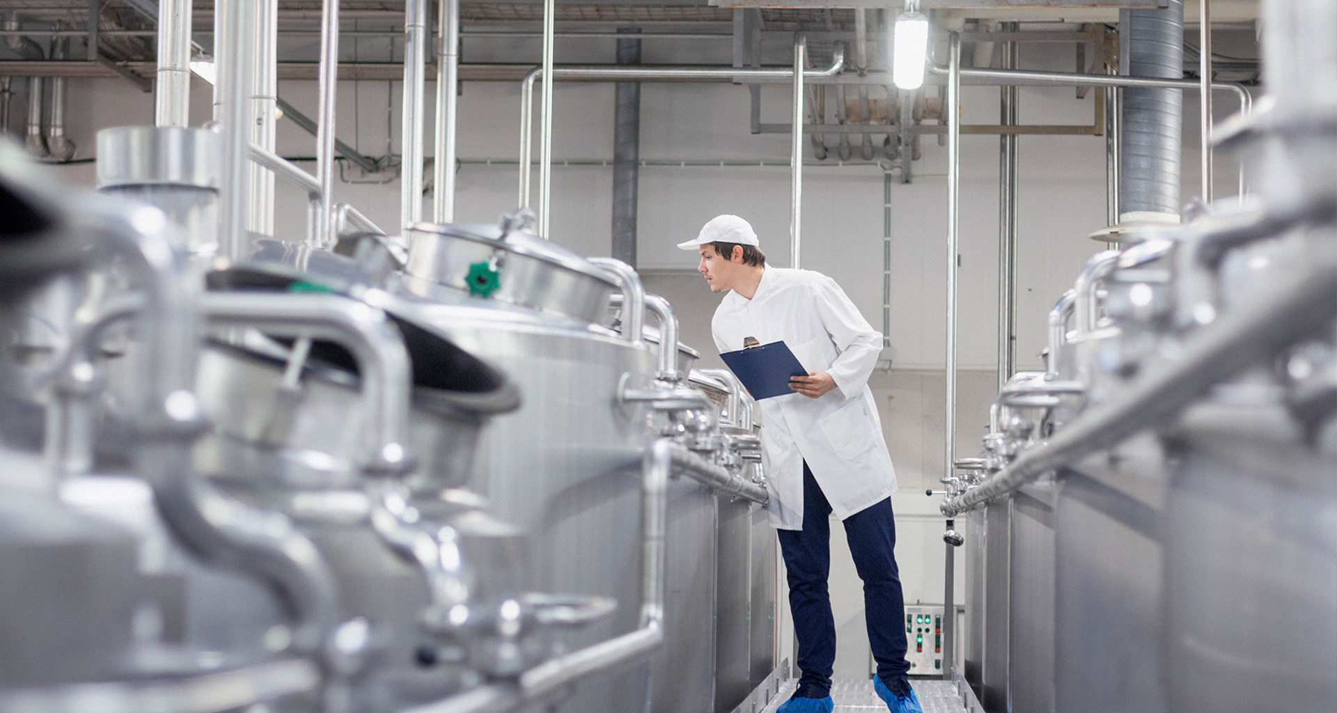 Arbejder inspicerer rustfri ståltanke i en industriel facilitet og holder en clipboard.