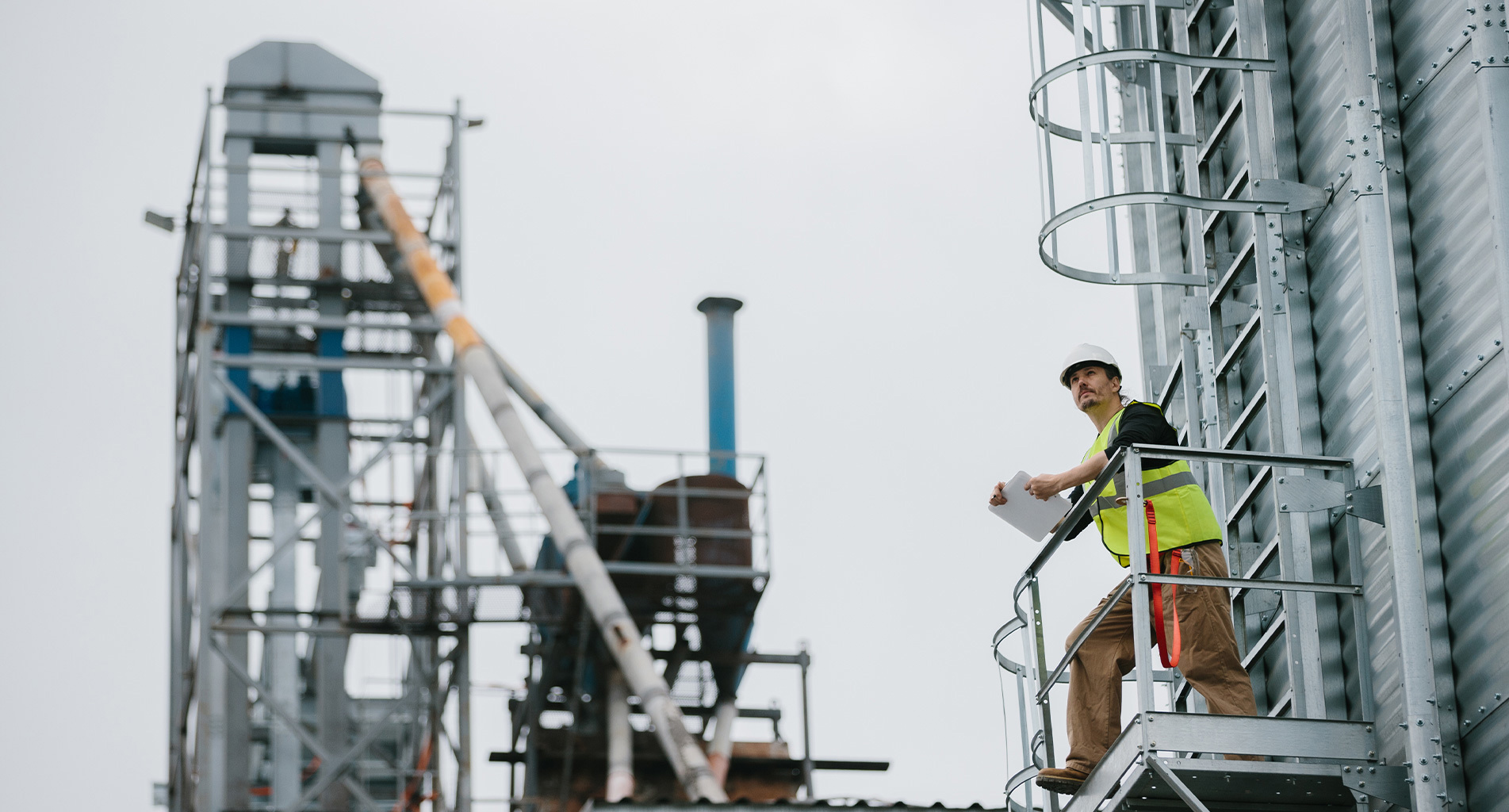 Bygningsarbejder i sikkerhedsudstyr inspicerer industristed fra hævet platform.