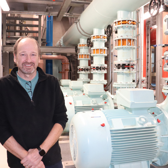 Mand står i en industriel facilitet med store pumper og rør i baggrunden.