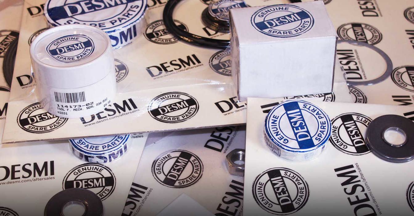 DESMI originale reservedele, herunder pakninger og etiketter, vist på et bord.