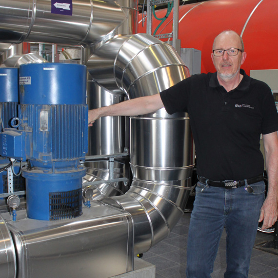 Mand står ved siden af industrielle pumper og rør i en facilitet.