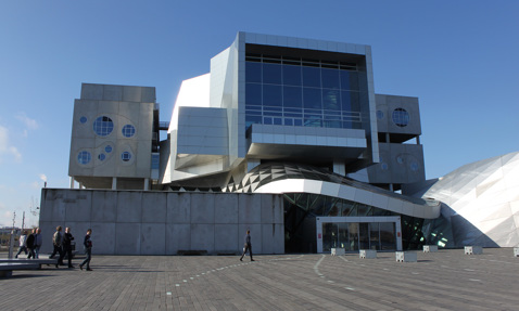 Moderne arkitektonisk bygning med geometrisk design og mennesker, der går i forgrunden.