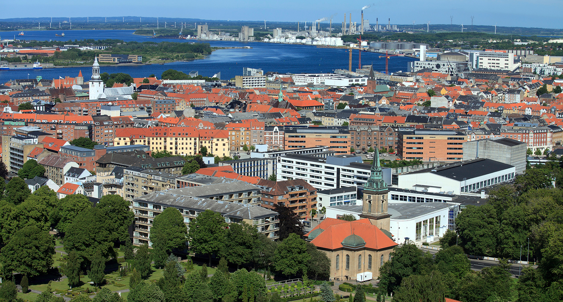 Luftfoto af en kystby med rødt tagede bygninger og industriel baggrund.