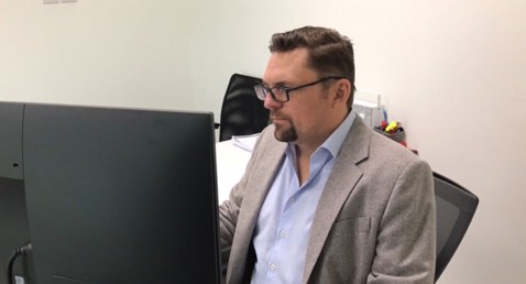 Mand med briller og blazer arbejder ved en computer på et kontor.