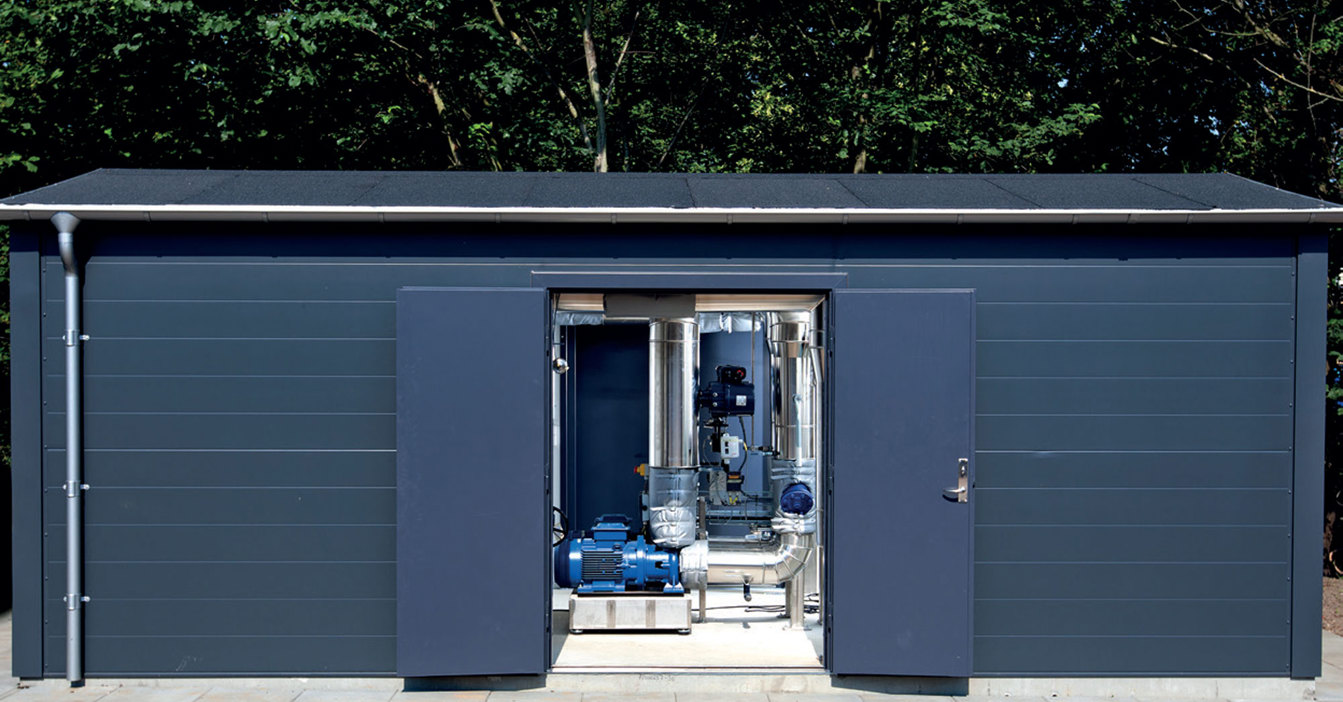 Lille blåt bygning med åbne døre, der afslører industrielle pumper og rør indeni.
