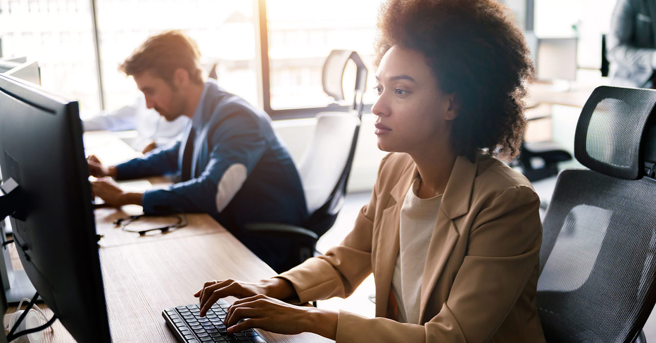 To professionelle arbejder ved computere i et lyst, moderne kontormiljø.