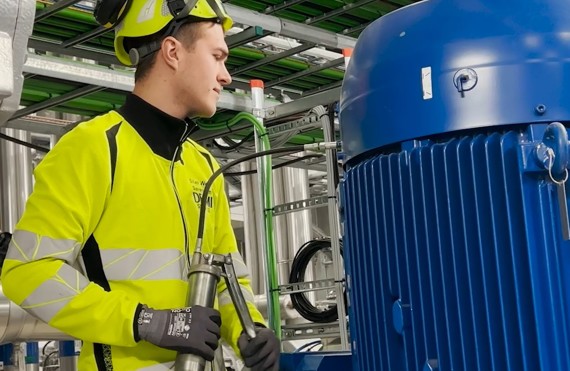 Tekniker i sikkerhedsudstyr inspicerer industrielt udstyr og holder en fedtpistol, DESMI synlig.