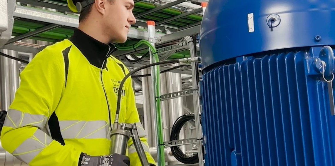 Tekniker i sikkerhedsudstyr inspicerer industrielt udstyr og holder en fedtpistol, DESMI synlig.