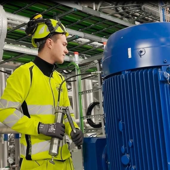 Tekniker i sikkerhedsudstyr inspicerer industrielt udstyr og holder en fedtpistol, DESMI synlig.