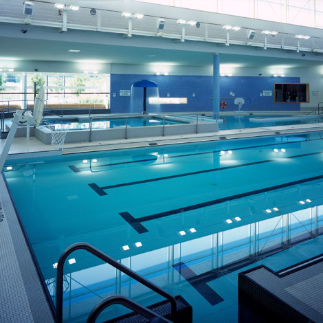 Indendørs swimmingpool med vipper, basketballkurv og kraftig loftbelysning.