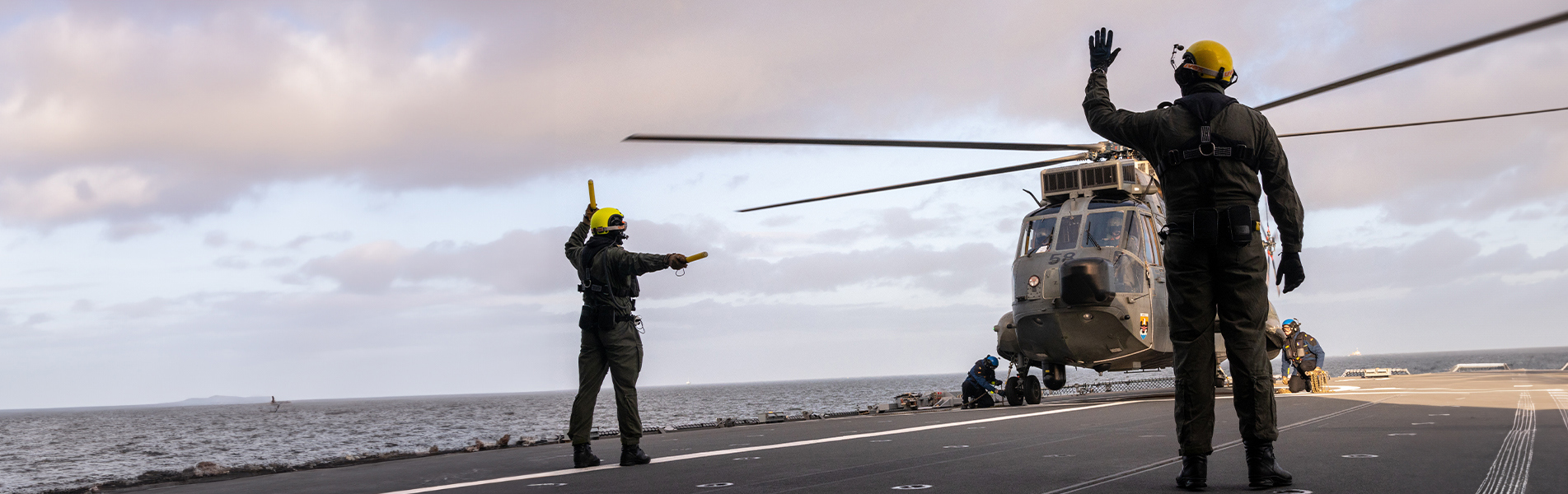 Flydækbesætning guider helikopterlanding på hangarskib til søs.