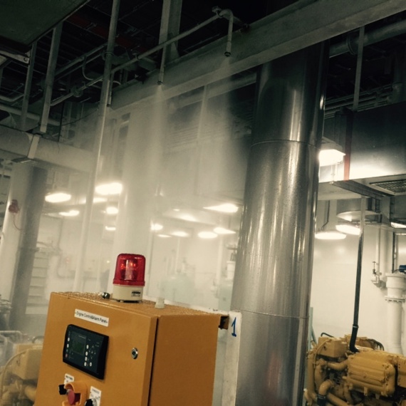 Industrielt rum med aktivt brandslukningssystem og kontrolpanel med rødt lys.