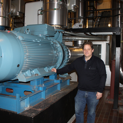 Mand står ved siden af en stor industriel pumpe i et maskinrum.