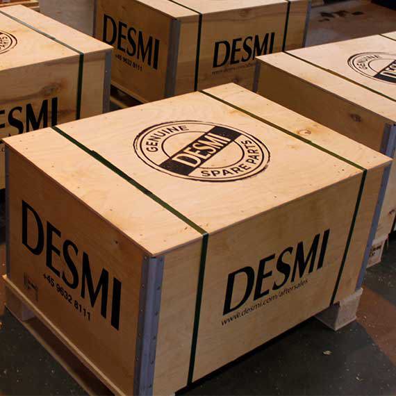 Trækasser mærket "DESMI Genuine Spare Parts" stablet på paller.