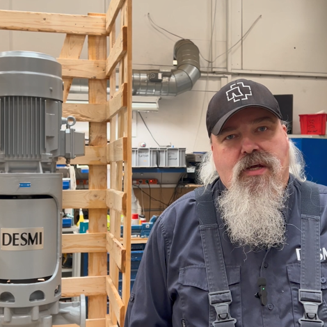 Mand står ved siden af en DESMI-pumpe i et industrielt værkstedsmiljø.