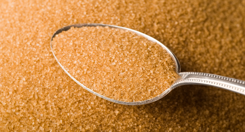 En skefuld brune sukkergranulat på en bunke løse sukkerkrystaller.