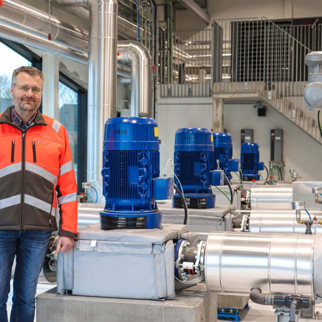 Mand i sikkerhedsvest ved siden af DESMI pumper til væskehåndtering i industriel omgivelser.